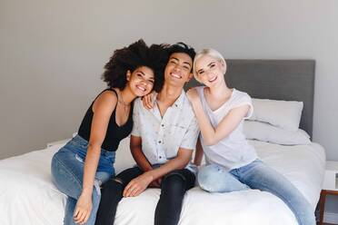 Happy young man and two female friends sitting on bed, portrait - ISF23279