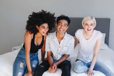 Young man and two female friends sitting on bed laughing - ISF23284