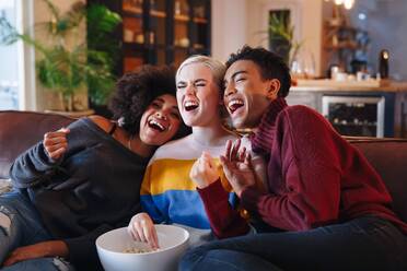 Junger Mann und junge Freundinnen lachen beim Fernsehen auf dem Wohnzimmersofa mit einer Schüssel Popcorn - ISF23344