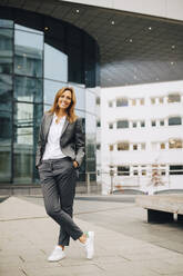 Full length of confident smiling businesswoman standing against glass building - MASF15036