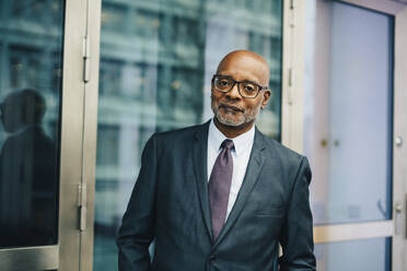 Portrait of confident senior businessman standing against glass door - MASF15043