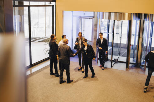 Kollegen schauen auf Geschäftsleute, die sich in der Büro-Lobby die Hände schütteln - MASF15049