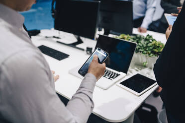 Midsection of businessman using smart phone at office desk - MASF15051