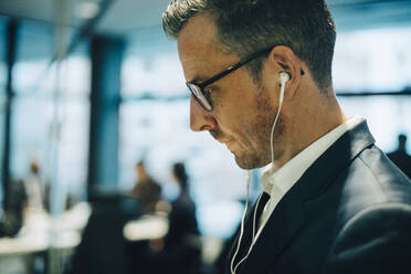Side view of mature businessman with eyeglasses wearing headphones at office - MASF15058