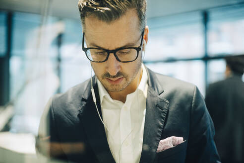 Älterer Geschäftsmann mit Brille, der Kopfhörer trägt und im Büro nach unten schaut - MASF15059