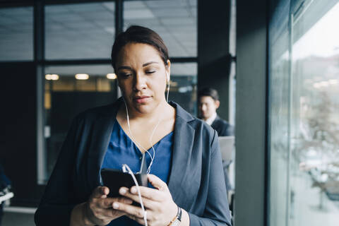 Geschäftsfrau, die ein Smartphone benutzt und über Kopfhörer im Büro hört, lizenzfreies Stockfoto