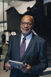 Porträt eines Geschäftsmannes im Anzug, der ein digitales Tablet hält, während er im Büro steht - MASF15105
