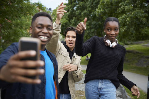 Glückliche Freunde schauen auf ihr Smartphone, während sie im Park tanzen - MASF15136