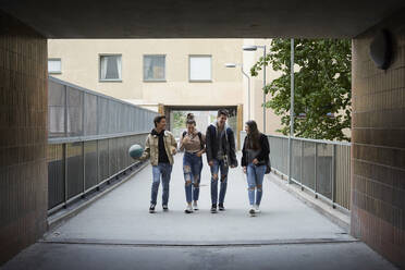 Volle Länge von glücklichen Freunden, die sich beim Gehen auf einer Fußgängerbrücke unterhalten - MASF15145