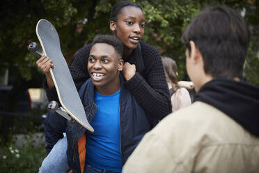 Lächelnder Teenager, der eine Freundin huckepack nimmt und ein Skateboard hält - MASF15152