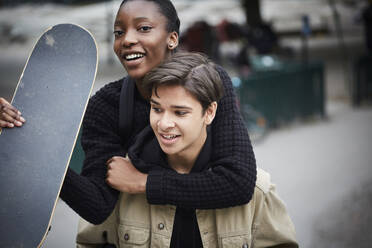 Junger Mann nimmt seine Freundin im Teenageralter mit dem Skateboard huckepack - MASF15154