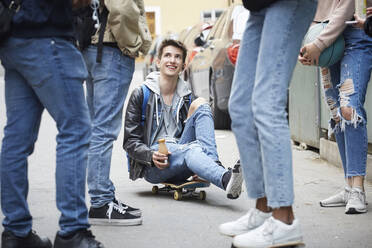 Niedriger Ausschnitt von Freunden, die neben einem lächelnden Teenager stehen, der auf einem Skateboard sitzt - MASF15161