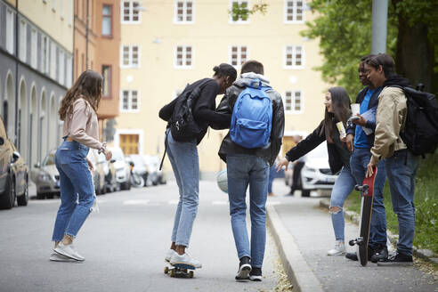 Teenager, der eine Frau beim Skateboardfahren unterstützt, während seine Freunde auf der Straße mit einem Ball spielen - MASF15164