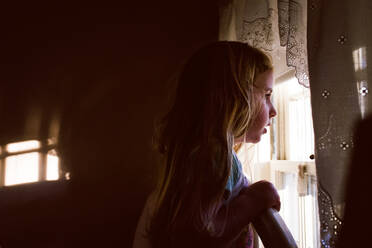 A little girl looks out a bedroom window. - CAVF69868