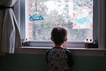 Ein kleiner Junge schaut in seinem Zimmer aus dem Fenster. - CAVF69870