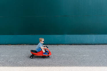 Ein kleiner Junge fährt mit einem roten Plasma-Auto vor einer grünen Wand. - CAVF69875