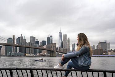 Attraktive junge Frau, die die Brooklyn Bridge vom Hudson River in New York City aus beobachtet - CAVF69891