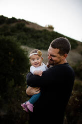 Vater umarmt seine kleine Tochter, während das Baby in die Kamera blickt - CAVF69905