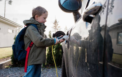 Kleiner Junge, der vor der Schule das Elektroauto der Familie ansteckt - CAVF69968