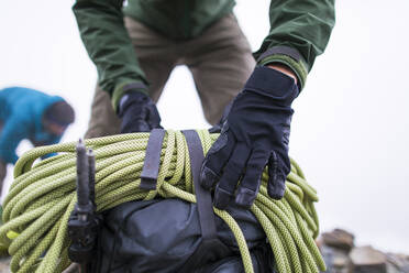 Ein Mann befestigt ein Seil an der Spitze seines Rucksacks. - CAVF69991