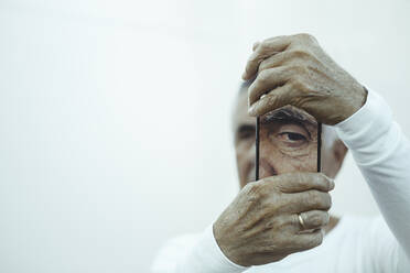 Älterer Mann, der sein Auge mit einem mobilen Gerät fotografiert - CAVF69998