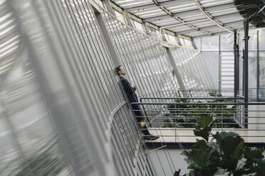 Businessman leaning against a glass wall in modern office building - JOSF03822