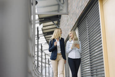 Zwei junge Geschäftsfrauen mit Tablet zu Fuß und im Gespräch in modernen Bürogebäude - JOSF03827