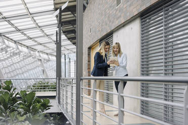 Two young businesswomen sharing tablet in modern office building - JOSF03829