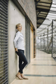 Junge Geschäftsfrau lehnt an einer Wand in einem modernen Bürogebäude - JOSF03830