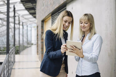 Zwei glückliche junge Geschäftsfrauen mit Tablet in einem modernen Bürogebäude - JOSF03832