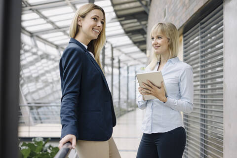 Zwei glückliche junge Geschäftsfrauen mit Tablet in einem modernen Bürogebäude, lizenzfreies Stockfoto