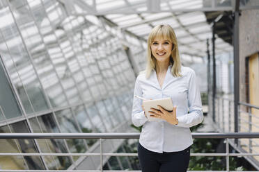 Portrait of a smiling young businesswoman in a modern office building using tablet - JOSF03841
