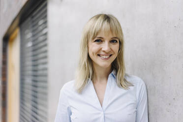 Portrait of a smiling young businesswoman leaning against a wall - JOSF03842