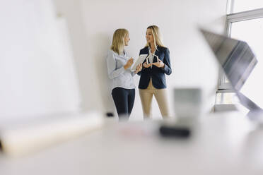 Zwei junge Geschäftsfrauen mit Tablet und Hausmodell im Gespräch im Büro - JOSF03860