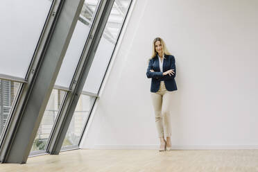 Portrait of a smiling young businesswoman leaning against a wall in a modern office building - JOSF03865