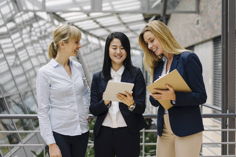 Drei Geschäftsfrauen mit Tablet im Gespräch in einem modernen Bürogebäude, lizenzfreies Stockfoto