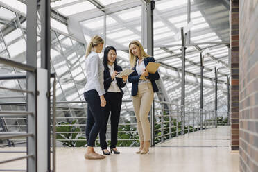Three businesswomen with tablet talking in modern office building - JOSF03876