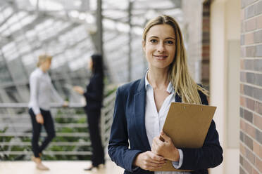 Portrait of a confident young businesswoman in a modern office building with colleagues in background - JOSF03879