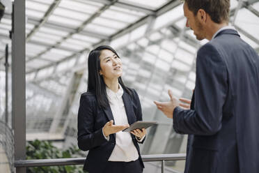 Businessman and businesswoman with tablet talking in modern office building - JOSF03894