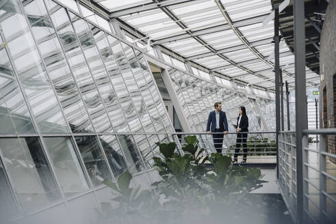 Businessman and businesswoman standing on a skywalk in modern office building - JOSF03897