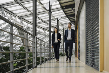 Geschäftsmann und Geschäftsfrau gehen in einem modernen Bürogebäude spazieren - JOSF03900