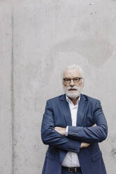 Portrait of serious senior businessman standing at a concrete wall - JOSF03951