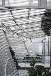 Businessman leaning against a glass wall in modern office building - JOSF03958