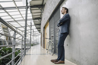 Businessman with closed eyes leaning against a wall in modern office building - JOSF04034