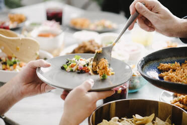 Cropped hand of man serving rice to female friend at dining table in party - CAVF70033