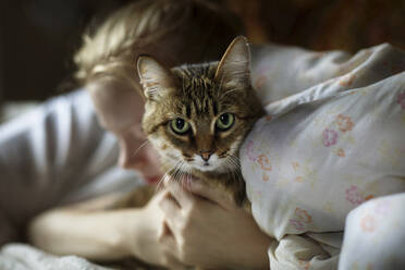 Frau umarmt Katze, während sie zu Hause auf dem Bett liegt - CAVF70050