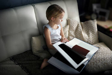 Hohe Winkel Ansicht des Mädchens Blick auf Farbe Swatch Buch, während auf dem Sofa sitzen - CAVF70051