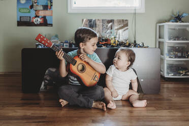 Kleiner Junge mit Gitarre und kleiner Schwester auf Hartholzboden sitzend - CAVF70085