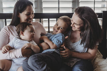 Familie mit zwei lachenden und kuschelnden Müttern zu Hause - CAVF70087