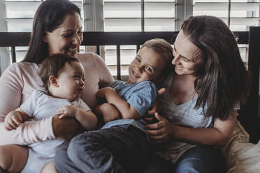 Family with two moms laughing and cuddling at home - CAVF70087